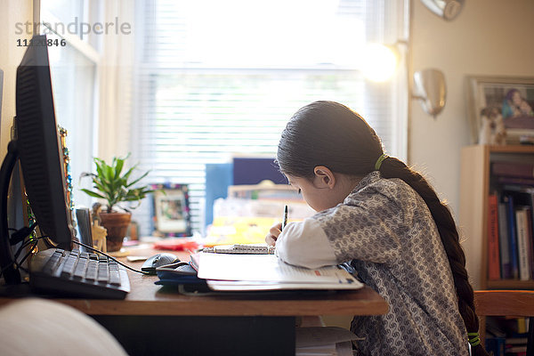 Gemischtrassiges Mädchen macht Hausaufgaben am Schreibtisch