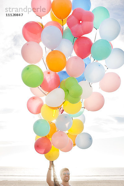 Kaukasischer Mann hält Luftballons am Strand