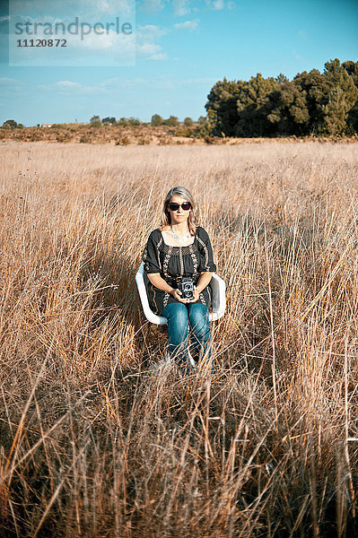 Kaukasische Frau sitzt mit altmodischer Kamera auf einem Feld