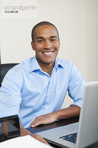 Lächelnder afroamerikanischer Geschäftsmann sitzt am Schreibtisch