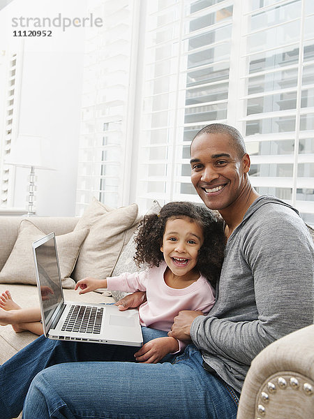 Vater und Tochter benutzen einen Laptop auf dem Sofa