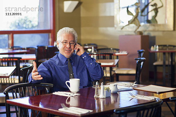 Hispanischer Café-Besitzer  der mit seinem Handy telefoniert