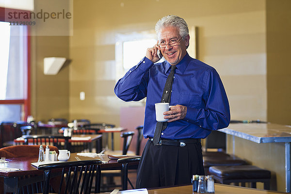 Hispanischer Café-Besitzer  der mit seinem Handy telefoniert