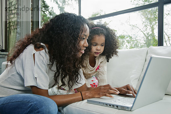 Gemischtrassige Mutter und Tochter benutzen gemeinsam einen Laptop