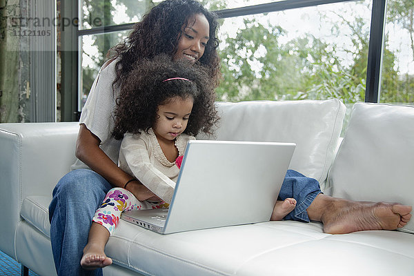 Gemischtrassige Mutter und Tochter mit Laptop auf dem Sofa