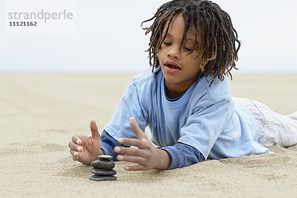 Gemischtrassiger Junge stapelt Steine auf Sand
