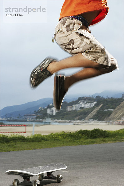 Mixed Race Junge springt über Skateboard