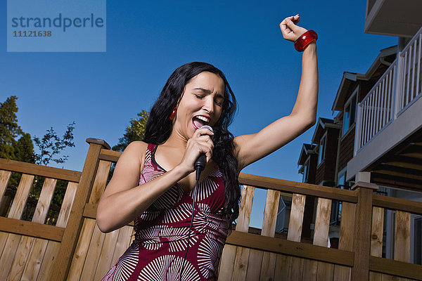 Hispanische Frau singt Karaoke im Hinterhof