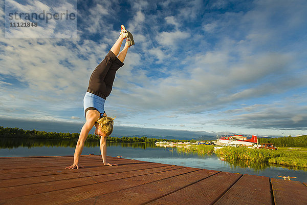 Kaukasische Frau übt Yoga am Steg auf einem stillen See  Anchorage  Alaska  Vereinigte Staaten