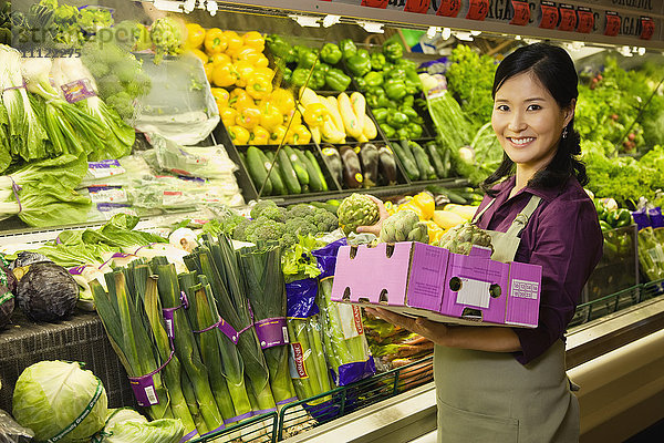 Asiatische Frau bei der Arbeit in der Gemüseabteilung eines Lebensmittelgeschäfts