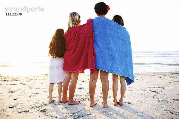 In Handtücher eingewickelte Mädchen stehen am Strand