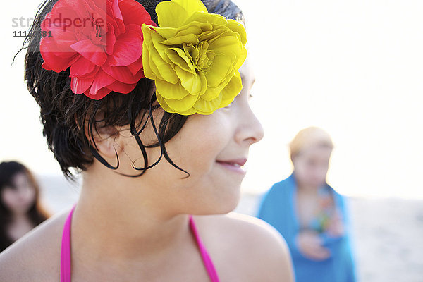 Gemischtrassiges Mädchen am Strand mit Blumen im Haar