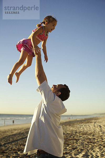 Vater hebt Tochter am Strand in die Luft