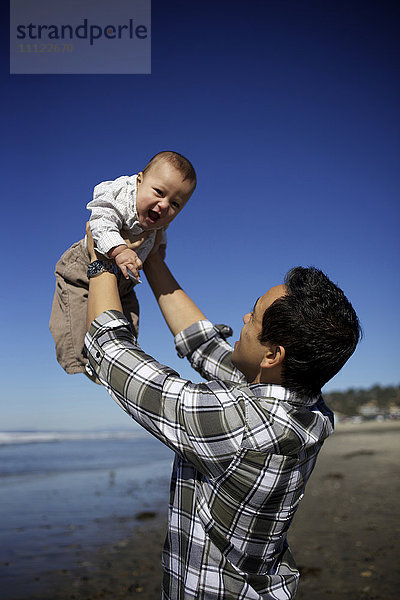 Vater hebt Baby am Strand hoch