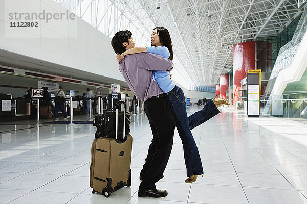 Asiatisches Paar  das sich im Flughafen umarmt