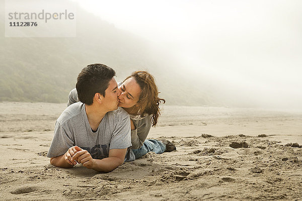 Hispanisches Paar küsst sich am Strand