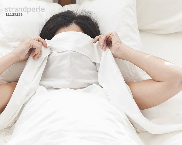 Hispanische Frau im Bett  die ihr Gesicht bedeckt