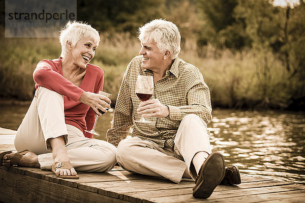 Älteres kaukasisches Paar trinkt Wein auf einem Holzsteg