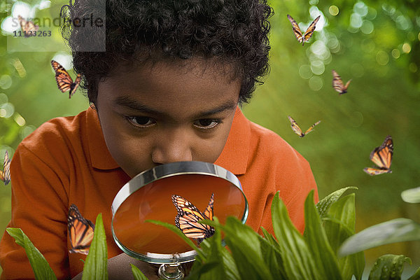 Afrikanischer Junge betrachtet Schmetterlinge mit einem Vergrößerungsglas
