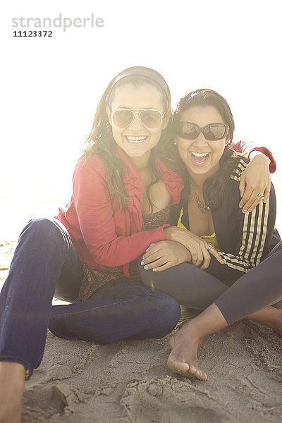 Lächelnde gemischtrassige Schwestern sitzen am Strand