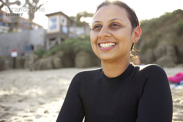 Lächelnde gemischtrassige Frau sitzt am Strand