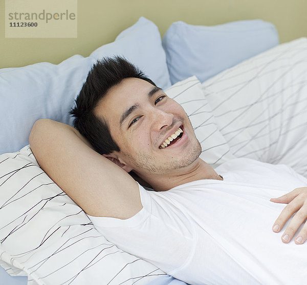 Lächelnder Mann gemischter Rasse  der im Bett liegt