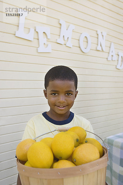 Gemischtrassiger Junge hält Korb mit Zitronen