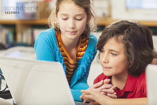 Kaukasische Kinder benutzen Laptop in der Bibliothek