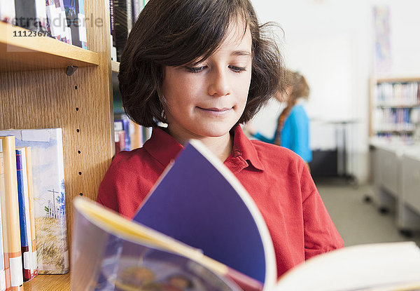 Kaukasischer Junge  der in der Bibliothek ein Buch liest