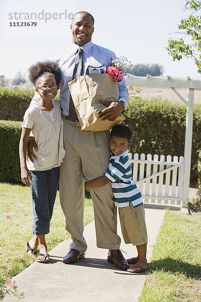 Afrikanischer Vater mit Lebensmitteln  der seine Kinder umarmt