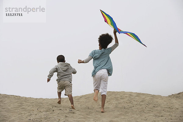 Gemischtrassige Kinder laufen am Strand mit Drachen