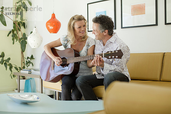 Mann bringt Frau im Wohnzimmer das Gitarrenspiel bei