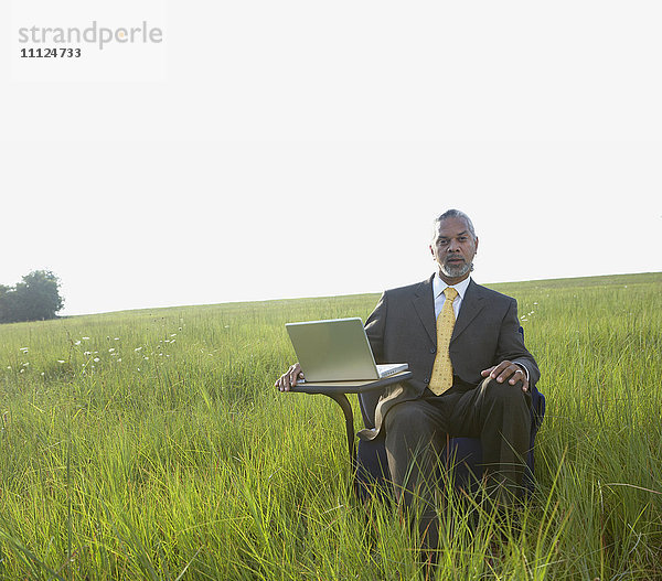 Afrikanischer Geschäftsmann sitzt mit Laptop auf einem Feld