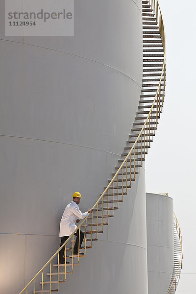 Kaukasischer Arbeiter  der eine Treppe auf einem Lagertank hinaufsteigt