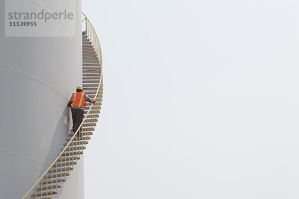 Gemischtrassiger Arbeiter steigt die Treppe auf dem Lagertank hinauf