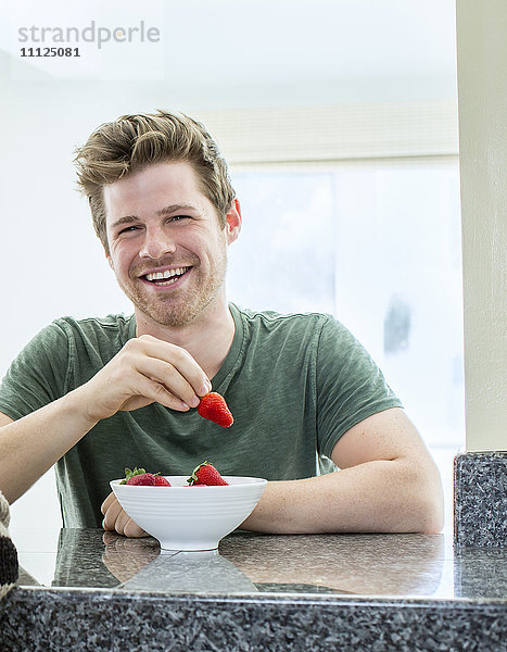 Mann isst Erdbeeren in der Küche