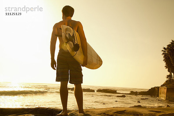 Mann trägt Surfbrett am Strand