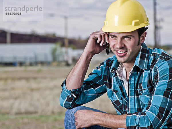 Lächelnder Bauarbeiter  der mit seinem Handy telefoniert