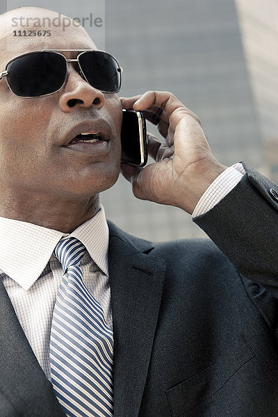 Schwarzer Geschäftsmann  der im Freien mit einem Handy telefoniert