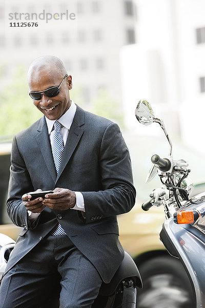 Schwarzer Geschäftsmann auf Motorroller sitzend  Textnachrichten schreibend