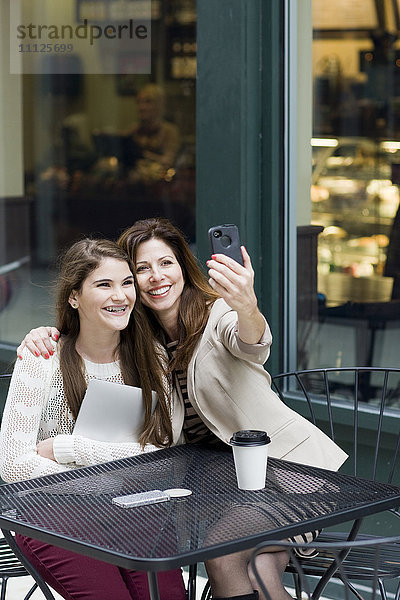 Kaukasische Mutter und Tochter beim Fotografieren in einem Cafe