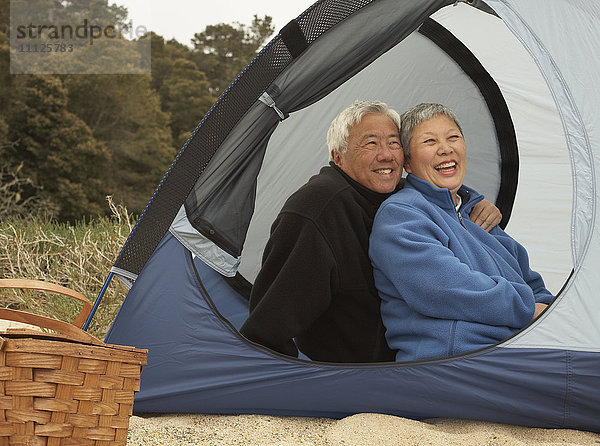 Älteres asiatisches Paar sitzt lächelnd im Zelt