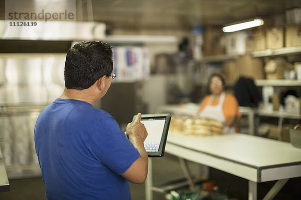 Hispanischer Bäcker mit Tablet-Computer in der Küche