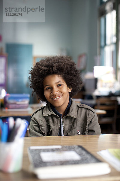 Afroamerikanischer Junge sitzt am Schreibtisch im Klassenzimmer