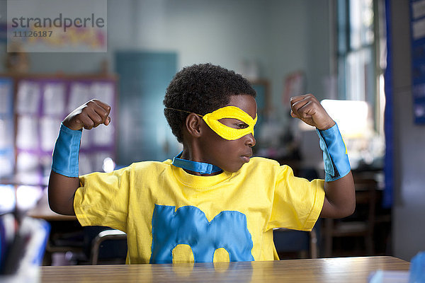 Afroamerikanischer Junge im Superheldenkostüm im Klassenzimmer