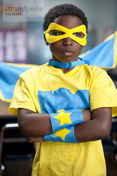 Afroamerikanischer Junge im Superheldenkostüm im Klassenzimmer