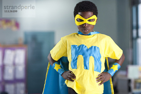 Afroamerikanischer Junge im Superheldenkostüm im Klassenzimmer