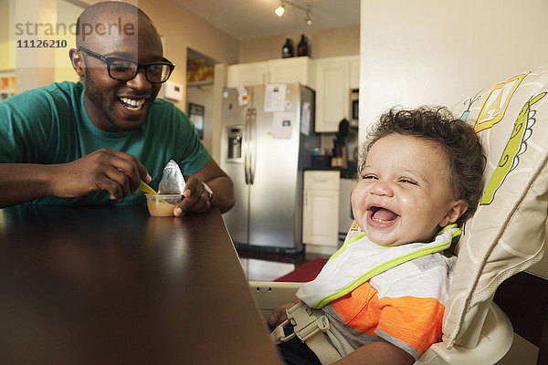 Vater füttert Baby am Tisch