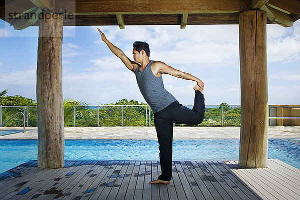 Asiatischer Mann übt Yoga am Pool
