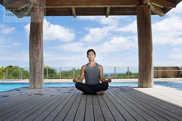 Asiatischer Mann übt Yoga am Pool